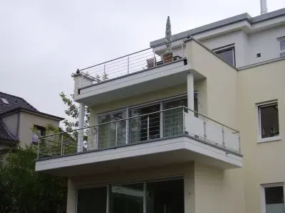 Modernes Einfamilienhaus mit großzügigem Balkon und Glasgeländer im Wohngebiet.