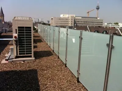 Glasgeländer als Sichtschutz auf einem Flachdach mit Kies und Klimaanlage in der Stadt.
