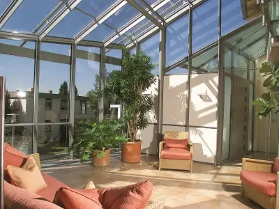 Heller Wintergarten mit großen Glasfenstern, modernen Möbeln und grünen Zimmerpflanzen.