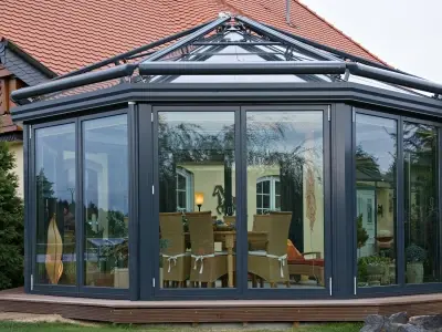 Moderner Wintergarten mit Glasfront und Aluminiumrahmen an Einfamilienhaus im Garten.