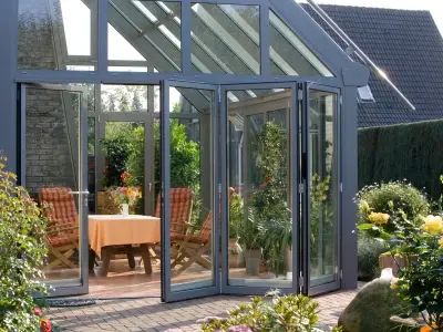 Moderner Wintergarten mit Glasfassade, Sitzgruppe und Blick auf gepflegten Garten.