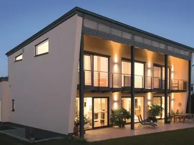 Modernes Einfamilienhaus mit Flachdach, großer Fensterfront und beleuchteter Terrasse.