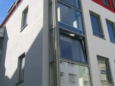 Moderne Fassade eines Mehrfamilienhauses mit großen Glasfenstern und Aufzugsschacht.