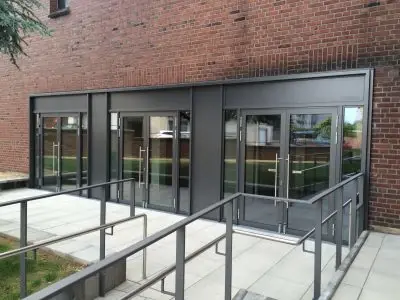 Barrierefreier Gebäudezugang mit Rampe und modernen Glastüren vor Backsteinwand