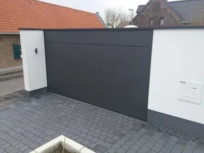 Moderne, elektrische Garagentor-Anlage mit anthrazitfarbener Oberfläche und Pflastersteinen.